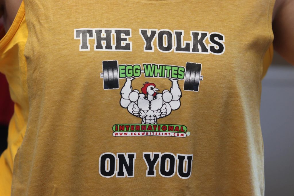 mustard yellow tank pump reading the yolks on you with egg whites international logo and cartoon muscular chicken lifting barbells