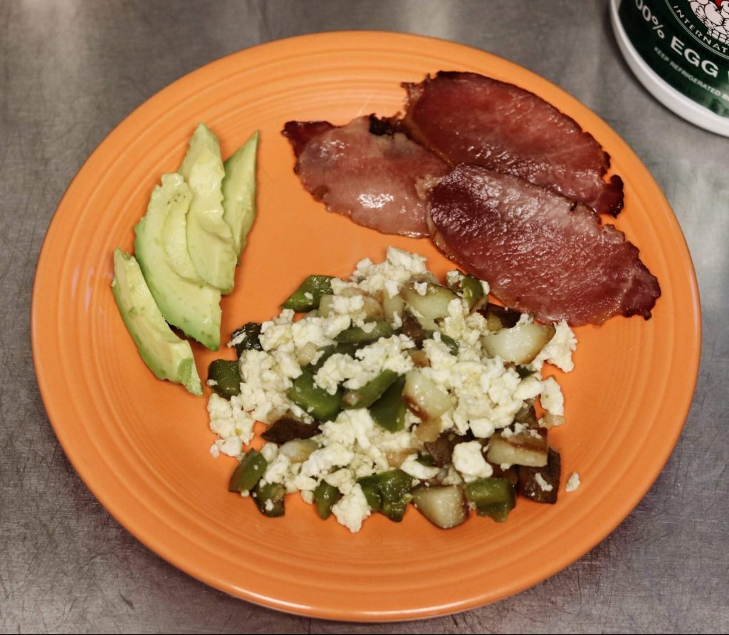 large orange plate with four slices of avocado, 3 slices of bacon, and pile of scrambled egg whites with potatoes, green peppers and mushrooms with corner of tub of egg whites international liquid egg whites in top right corner reading 100% egg