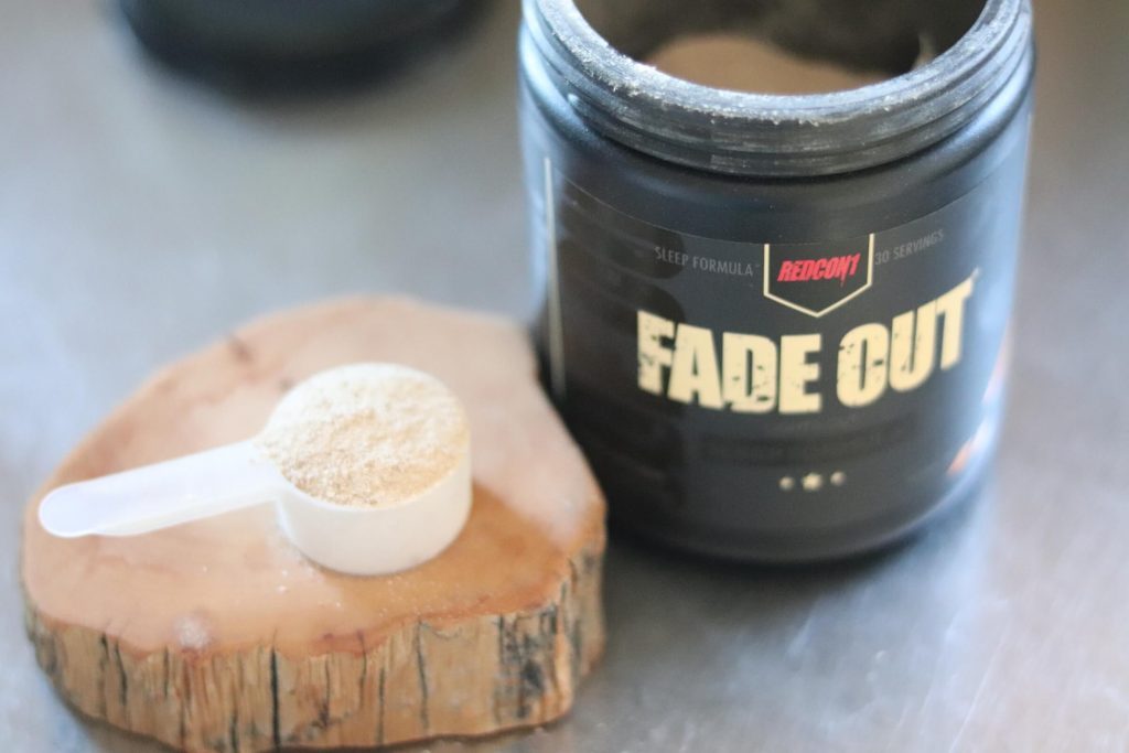open tub of redcon1 fade out next to wooden block holding scoop of fade out powder