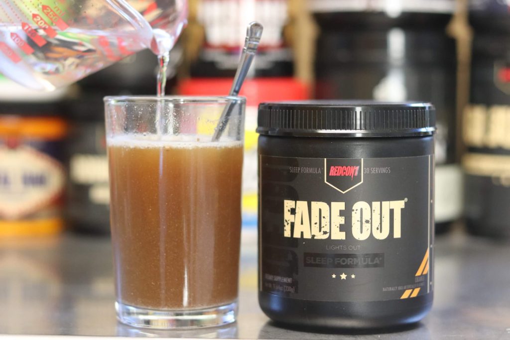redcon1 black tub of fade out lights out sleep formula next to glass filled with grainy mixture of water and fade out with measuring cup pouring in more water