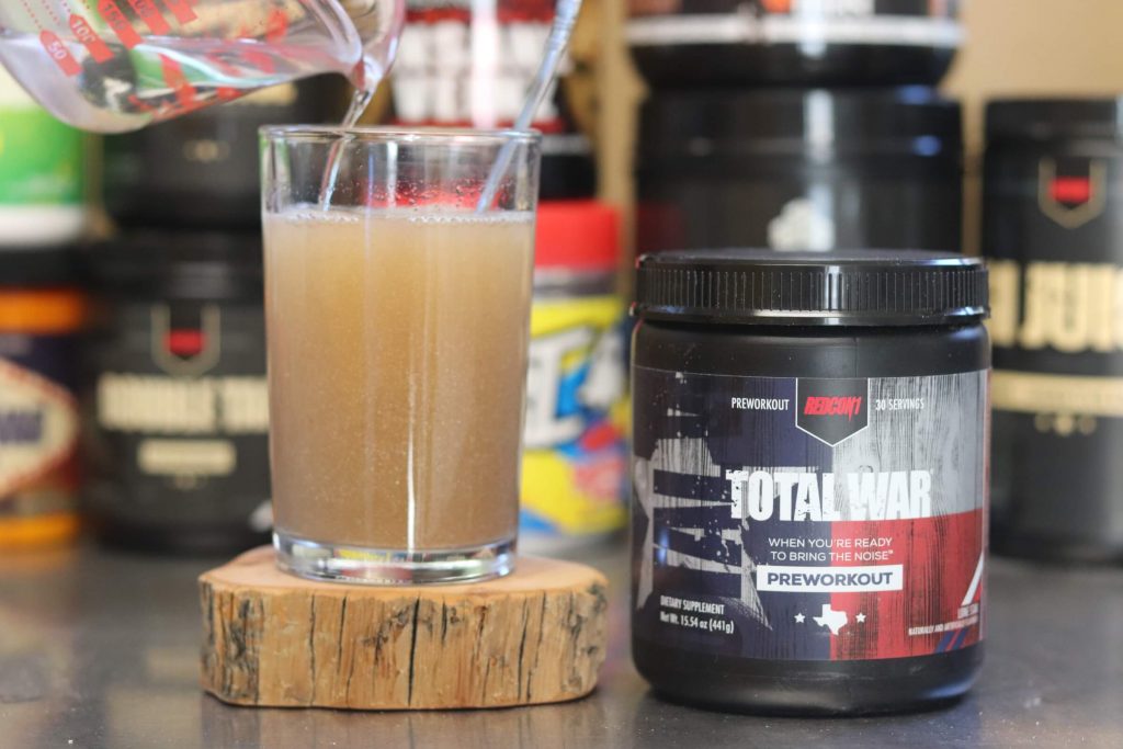 redcon1 total war lone star tub next to glass sitting on wood block holding water and total war mixture with measuring cup pouring in more water