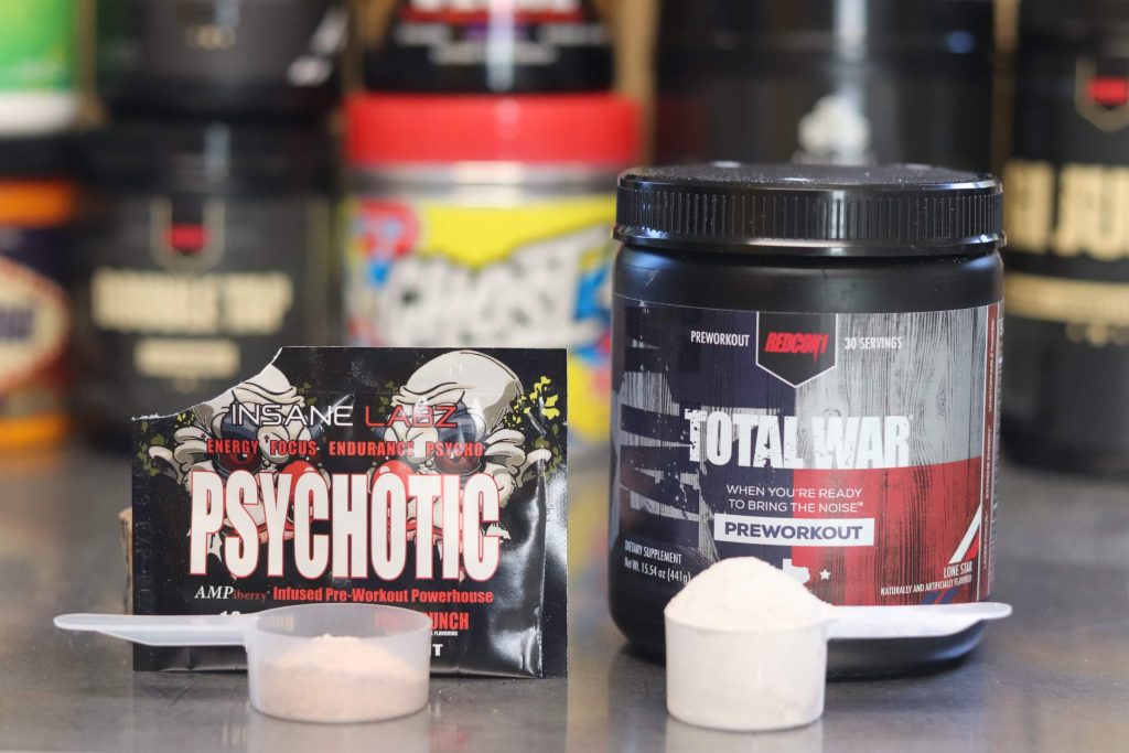 redcon1 total war pre-workout lone star tub with heaping scoop of white powder next to packet of insane labz psychotic fruit punch pre-workout with scoop of pinkish powder