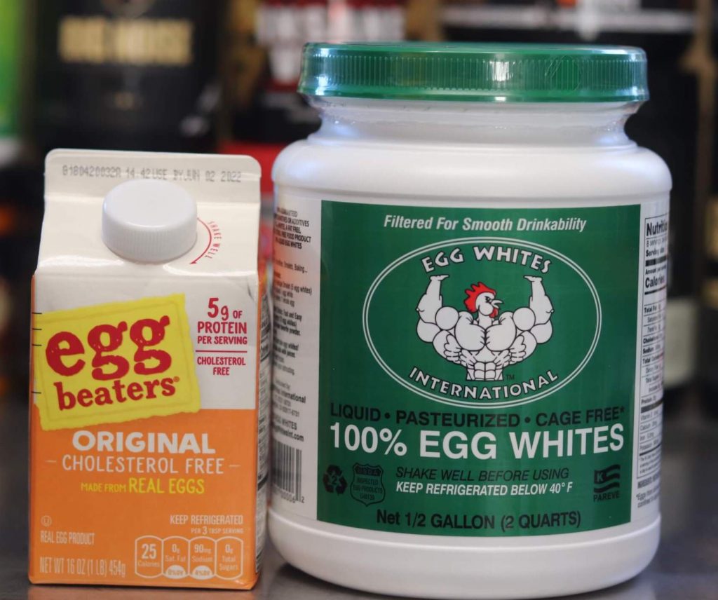 half gallon tub of egg whites international liquid egg whites with green label and muscular cartoon chicken, next to 16 ounce carton of egg beaters original cholesterol free real egg product with orange label
