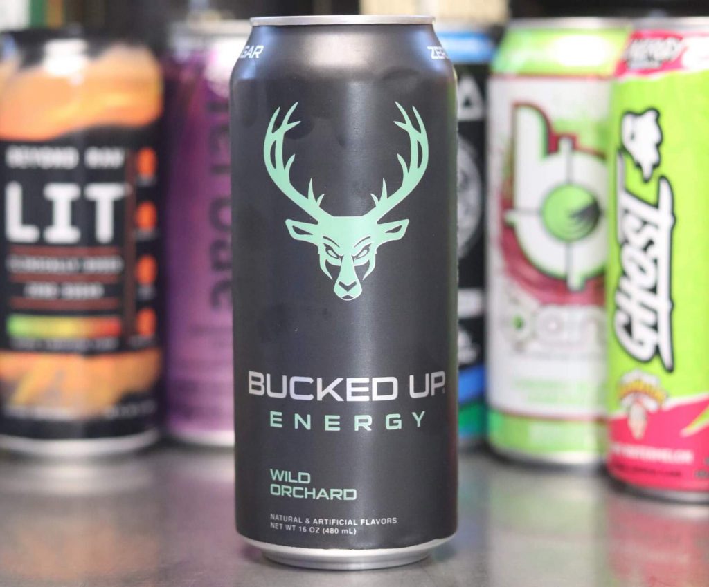 closeup of black can of bucked up energy wild orchard flavor with light green cartoon serious buck head and antlers with background of 5 other energy drink brands