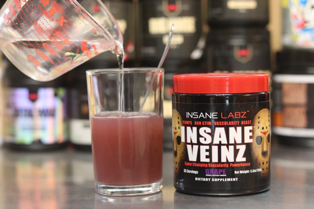 pyrex measuring cup pouring water into glass with purple liquid next to black tub of insane labz insane veinz grape pump formula