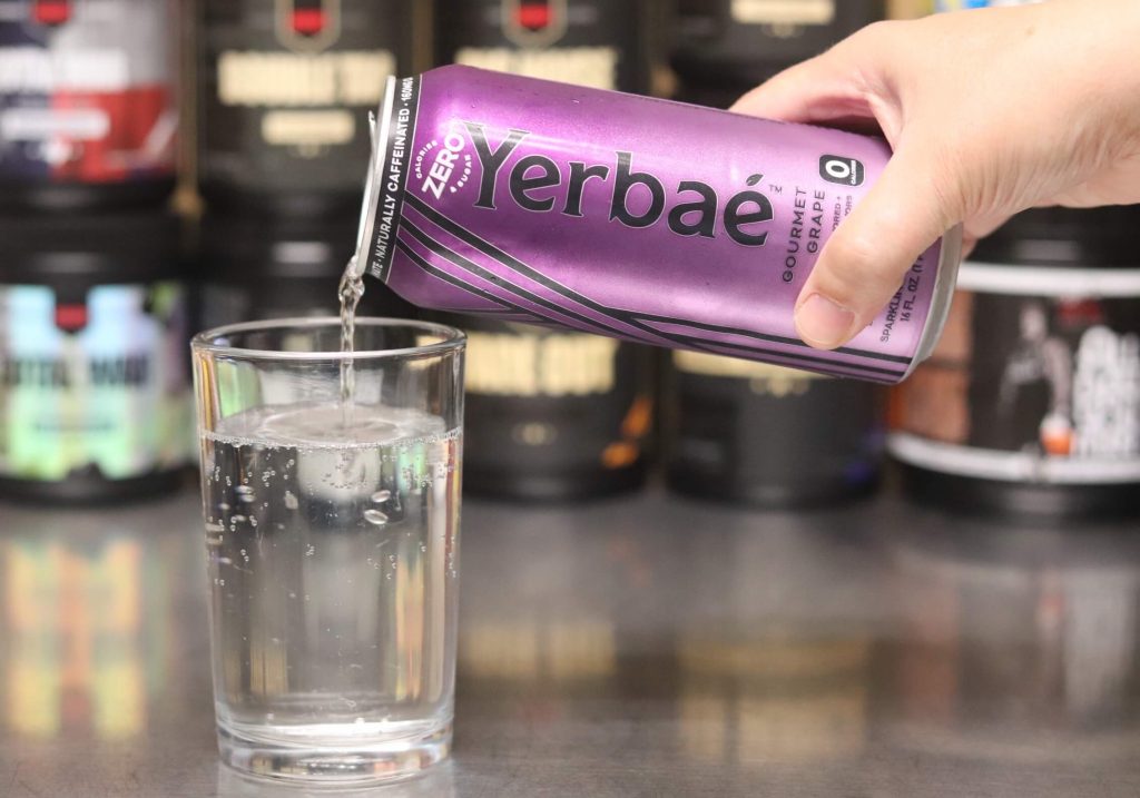 hand pouring purple can of clear carbonated yerbae fluid into clear glass