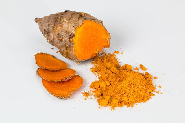 Large chunk of turmeric root next to sliced pieces of it and a pile of turmeric powder